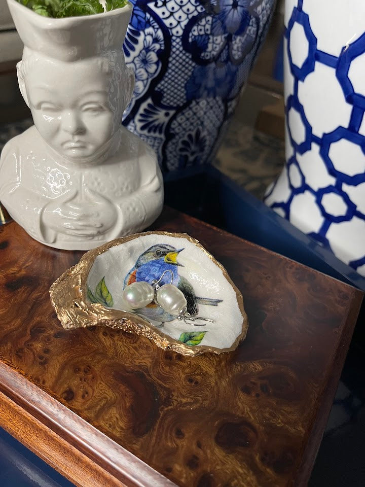 Decorative oyster shell with a painted scene on a wooden surface, surrounded by decorative vases.